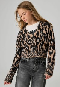 Beige und schwarze Leopardenmuster verkürzter Cardigan mit langen Ärmeln, Knopfverschluss und geripptem Saum, kombiniert mit dunkelgrauen Jeans.