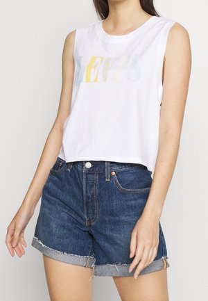 Biały bezrękawnik z kolorowym logo „LEVI'S”. W zestawie niebieskie szorty jeansowe z postrzępionym dołem i podwiniętymi mankietami.