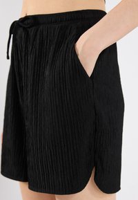 Black shorts with a textured, pleated design, featuring an elastic waistband and side pockets. The hem has a subtle curved shape.