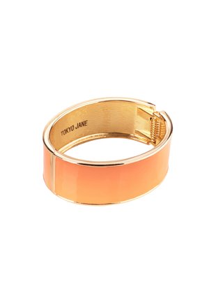 Gold-tone bangle bracelet with an orange enamel finish, smooth surface, and a clasp closure. Engraved brand name on the interior.