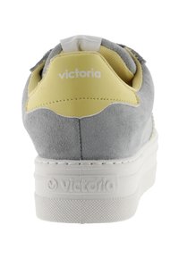 Sneaker in suede grigio con un dettaglio in pelle gialla sul tallone. Presenta una suola in gomma bianca e un logo embossato sul lato.