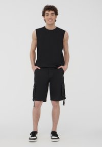 Top senza maniche nera abbinato a pantaloni cargo neri con tasche laterali e orli regolabili, completato da sneakers nere.