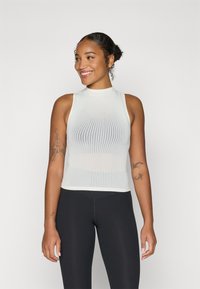 Top smanicato bianco a coste con collo alto, design aderente e tessuto testurizzato; abbinato a leggings neri a vita alta.