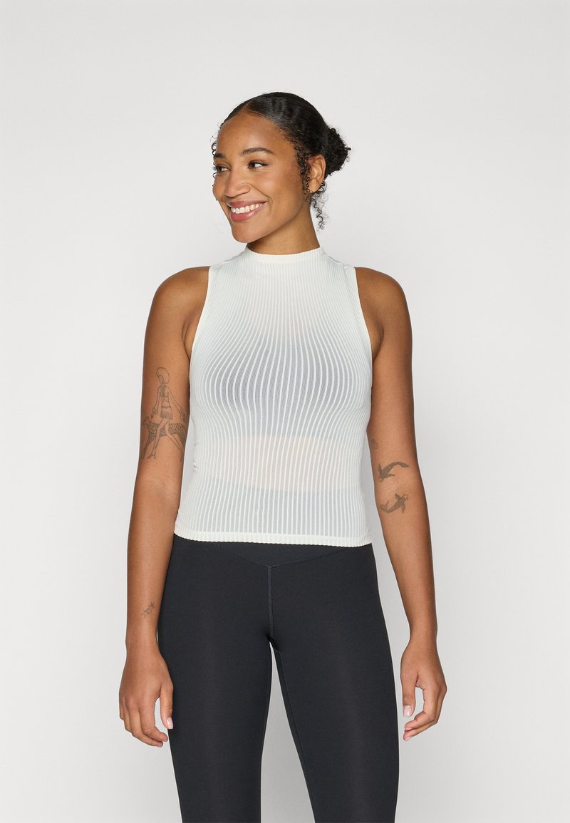 Top smanicato bianco a coste con collo alto, design aderente e tessuto testurizzato; abbinato a leggings neri a vita alta.