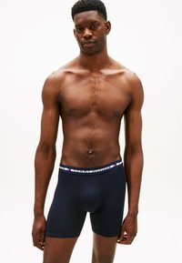 Tengerészeti boxer alsónemű, márkázott elasztikus derékpánttal, piros, fehér és kék kiegészítőkkel. Simító, rugalmas anyagból készült, szoros szabású.