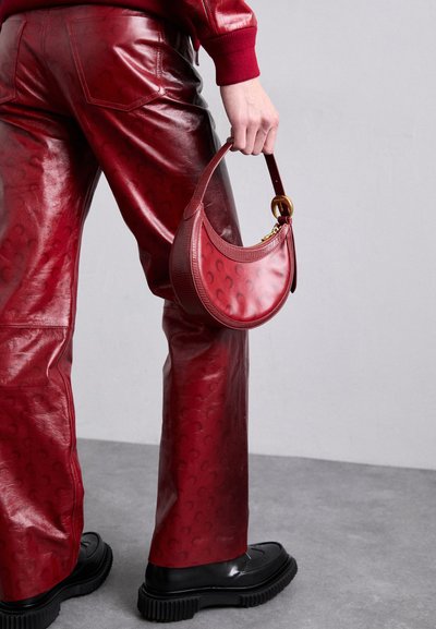 Pantalons en cuir rouge avec un motif en relief, associés à un sac rouge assorti. Le sac présente un design incurvé et un accent en métal doré. Chaussures noires à semelles épaisses.