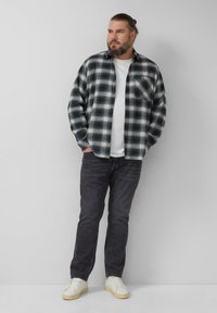 Camicia di flanella a quadri nera e bianca, indossata sopra una t-shirt bianca, abbinata a jeans scuri e sneakers bianche. Vestibilità robusta e rilassata.