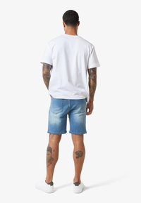 Jeansshorts in hellblau mit ausgeblichenen Akzenten, kombiniert mit einem schlichten weißen T-Shirt. Weiße Sneaker vervollständigen das lässige Outfit.