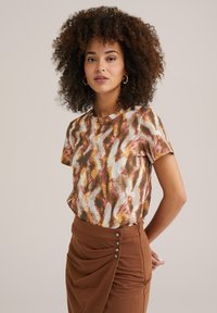 Short-sleeve top in a multicolored abstract pattern featuring shades of brown, cream, and pink. Smooth fabric with a relaxed fit.