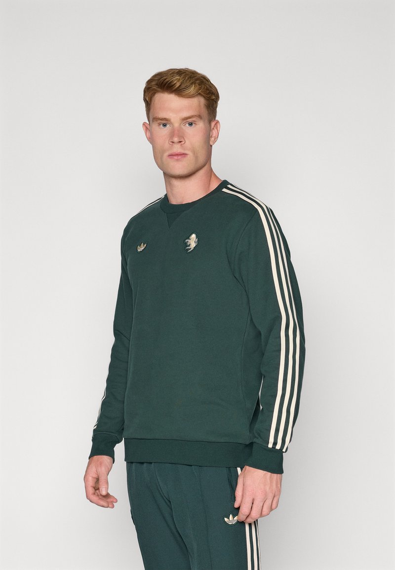 Grøn sweatshirt med cremefarvede striber på ærmerne, rund halsudskæring og broderet logo på brystet. Blødt stof med en afslappet pasform.