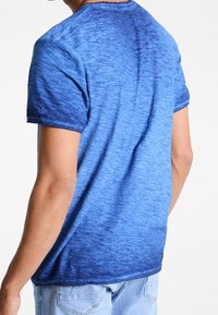 Niebieska koszulka z gradientem, z krótkimi rękawami, charakteryzująca się miękką teksturą i okrągłym dekoltem. Dolna część przechodzi w ciemniejszy odcień niebieskiego.