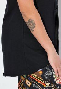 Sort kortærmet top med krum kant, parret med mønstrede leggings i livlige farver og geometriske designs.