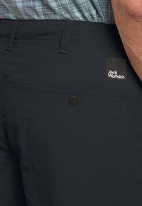 Shorts blu scuro realizzati in tessuto leggero, dotati di una tasca laterale con chiusura a scatto nera e un'etichetta con il logo Jack Wolfskin.