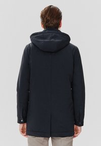 Granatowa wodoodporna parka z kapturem, długimi rękawami i prostym krojem. Posiada mankiety na zatrzaski i tylny wentyl. Gładkie wykończenie tekstylne.