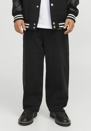 Person iført sorte jeans med vide ben, sorte læderloafers, hvid T-shirt og sort varsityjakke med stripede manchetter og kant.