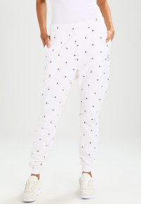 Vita träningsbyxor med lös passform, prydda med ett mönster av små svarta och röda trianglar. Elastisk midja och muddar. Slät tygtextur.