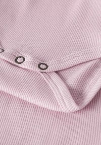 Svetlo roza rebrasta tkanina z nežno teksturo, z črnimi pritiskači vzdolž izreza in prepognjenim robom.