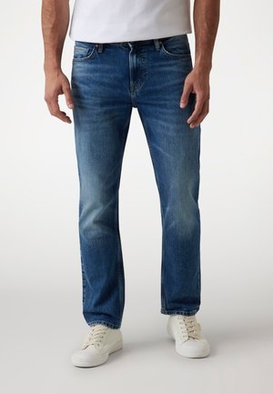 Blue denim jeans featuring a straight leg design, light fading, five-pocket detail, and reinforced stitching at the hem, paired with white shoes.