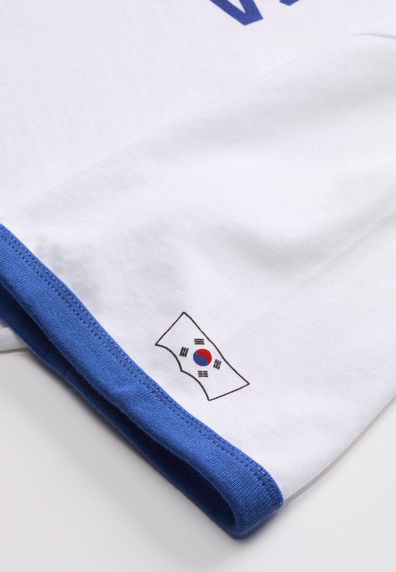 Manche blanche avec ourlet bleu comportant un petit drapeau sud-coréen imprimé près du bord du tissu.