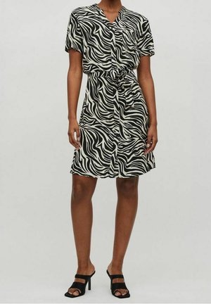 Femme portant une robe à manches courtes imprimée zèbre noir et blanc avec une ceinture à la taille, associée à des sandales à talons noires à bout ouvert.