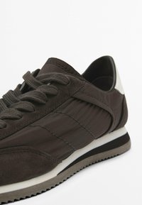 Scarpe sportive marroni con una combinazione di suede testurizzato e tessuto liscio, lacci rotondi, un accento bianco sul tallone e suola in gomma testurizzata.