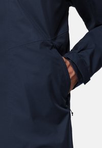 Navy blue jacket with a smooth, matte texture. Features a side pocket, elastic cuffs, and a straight cut design. Minimalistic detailing.