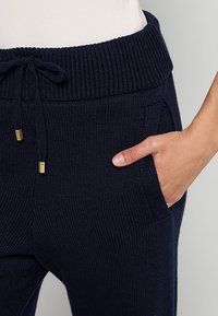 Marine gebreide joggers met een geribde tailleband, trekluiting en zijzakken; voorzien van kleine gouden accenten bij de uiteinden van de trekluiting.