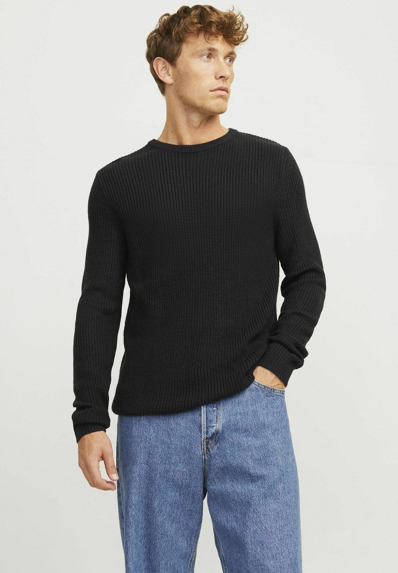 Black ribbed long-sleeve sweater with a crew neckline, paired with light blue loose-fitting jeans. Textured fabric and fitted cuffs.