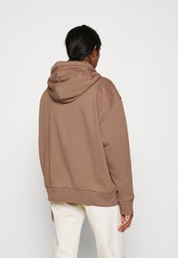 Sweat à capuche surdimensionné de couleur brun clair, fabriqué en tissu doux. Comprend une capuche avec cordon de serrage, un ourlet côtelé et des manches larges pour une coupe décontractée.