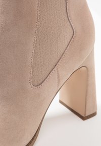 Botín beige de ante con paneles laterales elásticos, tacón ancho y textura lisa. Presenta detalles cosidos a lo largo de las costuras.