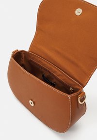 Bruine crossbodytas van synthetisch leer met een gouden druksluiting, witte stiksels en een enkele binnenzak. Gevoerd met gladde stof.