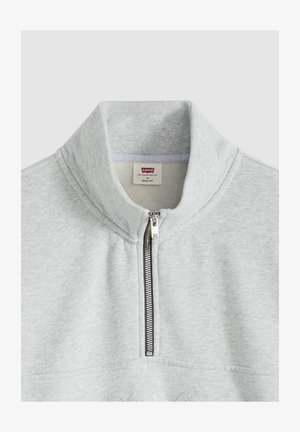 Sweat-shirt léger gris clair avec col montant, fermeture éclair à moitié, et détail brodé subtil à l'avant. Matière douce en mélange de coton.