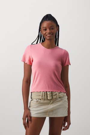 Haut rose à manches courtes côtelé avec un ourlet festonné, associé à une mini-jupe beige clair avec une large ceinture.