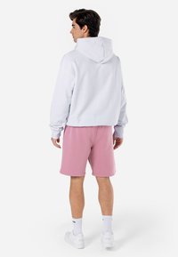 Um hoodie cinza claro com capuz, combinado com calções cor de rosa. O hoodie tem mangas longas e um corte descontraído, aumentando o conforto e a mobilidade.