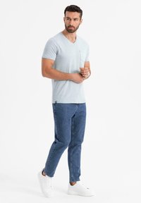 Světle modré tričko s krátkým rukávem a výstřihem do V, se spodní kapsou, v kombinaci s tmavě modrými zúženými džíny a bílými teniskami.