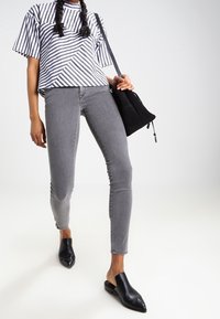 Femme portant une chemise rayée noir et blanc, un jean skinny gris, des mocassins en cuir noirs, et portant un sac à épaule noir.