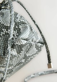 Geantă texturată cu imprimeu de șarpe alb-negru, cu un design strâns, prezentând o curea împletită și accente din hardware metalic.