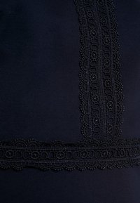 Námořnická tkanina s intricate černou krajkou na výstřihu a lemu, s texturovaným vzorem smyček a květinovými akcenty.