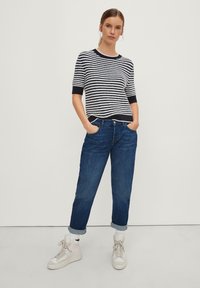 Maglione a righe in blu navy e bianco, maniche corte, abbinato a jeans blu con risvolto e sneakers bianche con dettagli testurizzati.