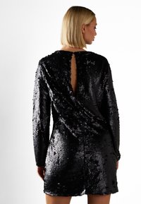 Svart paljettklänning med långa ärmar och en djup öppning i ryggen, med en omslagdesign och slät textur.