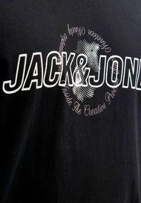 Must mustriga kangas, millel on julge valge tekst "JACK & JONES" täpilise kaardi kohal ning selle ümber kumer joonistus.