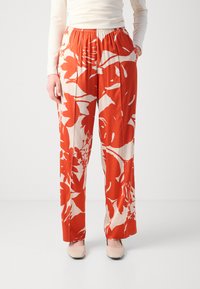 Red and cream floral print trousers with an elastic waistband, wide-leg design, and soft fabric. Pockets are included on each side.