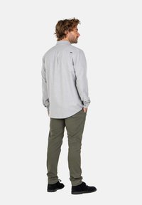 Camisa gris de botón con dobladillo redondeado, combinada con pantalones verde oliva y zapatos negros. La camisa presenta un canesú en la parte posterior y puños abotonados.