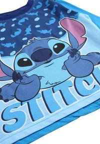 T-shirt bleu présentant un personnage de dessin animé avec de grands yeux et oreilles, entouré d'un motif de personnages plus petits, étiqueté "STITCH".