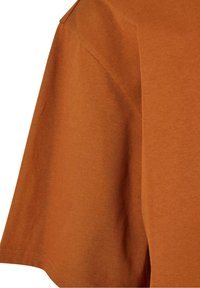 Manche et partie avant supérieure d’un t-shirt en coton à manches courtes couleur rouille avec des détails de couture visibles.