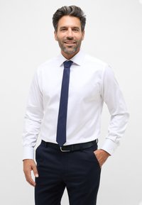 Weißes Hemd mit langen Ärmeln, kombiniert mit einer dunkelblauen strukturierten Krawatte und navyblauen Trousers. Verfügt über einen klassischen Kragen und Knopfmanschetten.