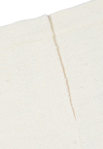 Gros plan sur un tissu tissé couleur crème avec un motif discret en forme de grille et de petits points en relief, présentant une couture au centre.
