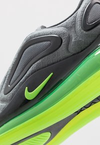 Nike-sneaker med en grå texturerad överdel, svarta accenter och en grön genomskinlig luftsåle. Anmärkningsvärd swoosh-logotyp i livlig grön.