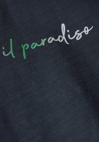Tissu marine présentant un texte brodé blanc et vert qui dit "il paradiso". La texture semble douce et légèrement tissée.