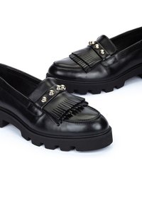 Mocasines de cuero negro con un acento de flecos, adornados con tres esferas metálicas y una suela texturizada gruesa.